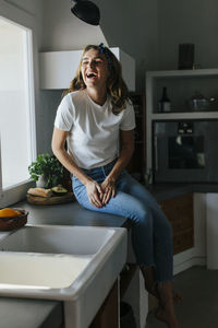 Happy woman sitting on kitchen cupboard