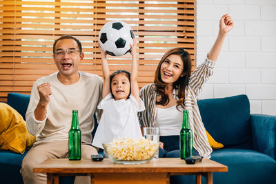 Portrait of smiling friends using phone while sitting on sofa at home