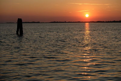 Silhouette person standing in sea against sky during sunset