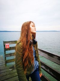 Young woman standing by railing on pier against sky