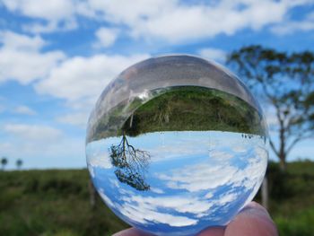 Upside down image of hand holding crystal ball against sky