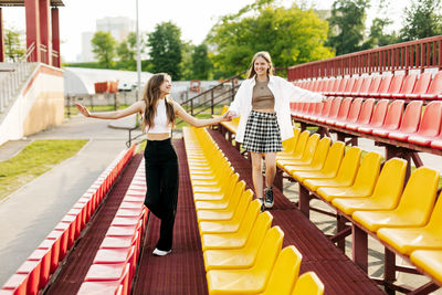 Two teenage girls walk together through the stands of the school stadium, talking, holding hands