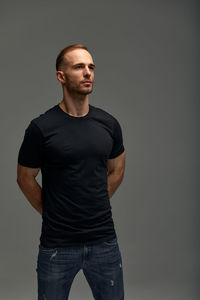 Portrait of young man standing against black background