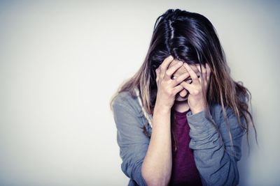 Depressed woman covering face against gray background