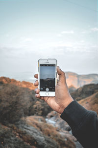 Close-up of hand holding smart phone against sky