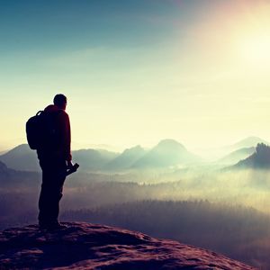 Silhouette of photographer overlooking a blanket of fog over valley to sun