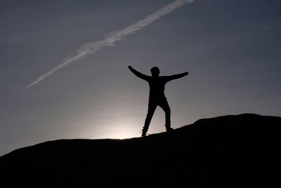 Silhouette man with arms outstretched standing against sky