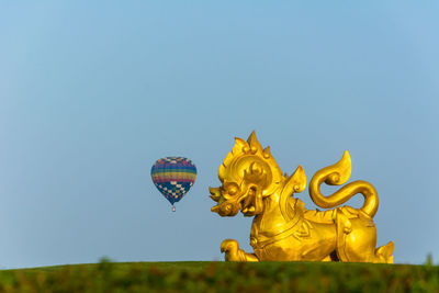 Golden statue with parachute against clear blue sky