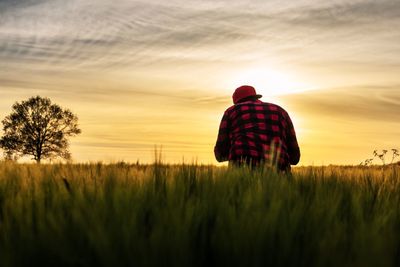 Rear view of man standing on field against sky at sunset