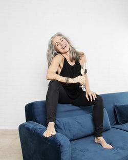 Cheerful mature woman sitting with glass of champagne on sofa at home