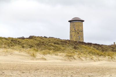 Lighthouse on beach by building against sky