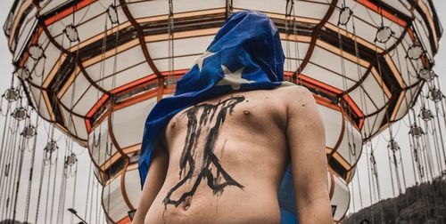 Shirtless man standing with face covered by flag
