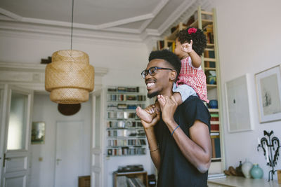 Smiling young man carrying playful daughter at home