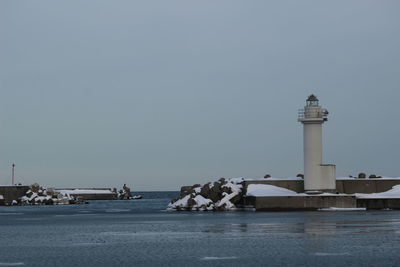 Lighthouse on building by sea against clear sky