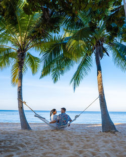 Rear view of couple sitting on hammock at beach