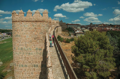 Avila, spain. people on pathway over stone thick wall with large towers encircling avila