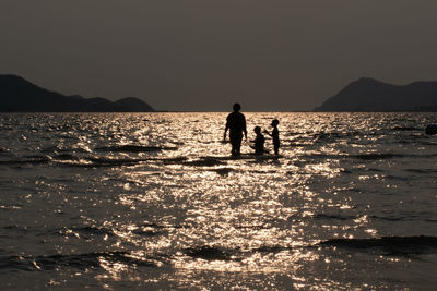 Silhouette men in sea against sky during sunset