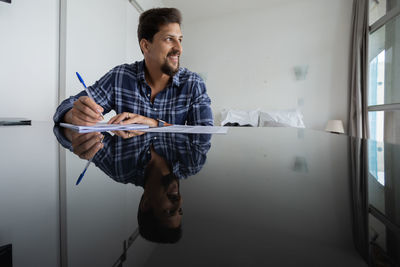 Young man working at home signing papers smiling 