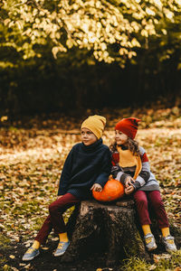 A little girl and a boy children are sitting on a tree stump with a large pumpkin in an autumn park