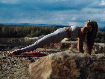 Young beautiful blond woman with long hair in activewear doing yoga pose in outdoor training in hill