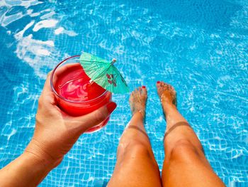 Low section of woman holding drink in swimming pool