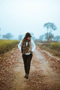 Man standing on road amidst field against sky