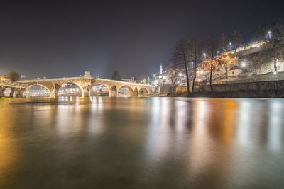 Illuminated bridge over river against sky at night