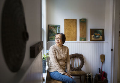 Thoughtful woman looking away while sitting by window at home