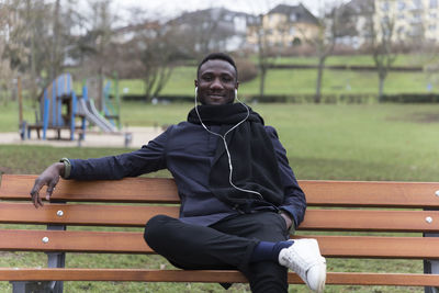 Portrait of smiling man listening music while sitting on bench in park