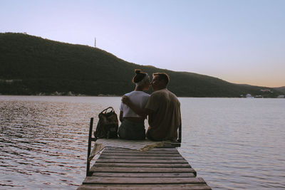 Rear view of couple sitting on lake against sky