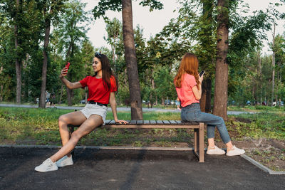 Young women using mobile phone while sitting on bench at park