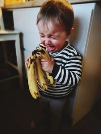 Cute girl with banana crying while standing in kitchen