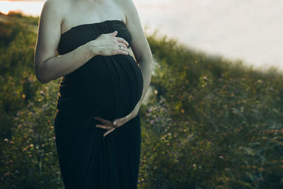 Pregnant woman hugging her tummy standing outdoors surrounded by nature. pregnancy, expectation