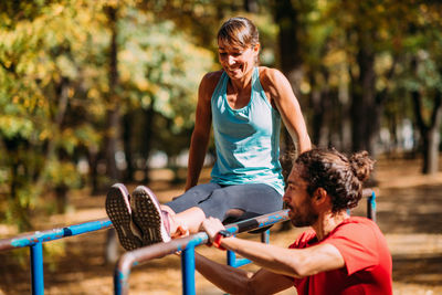 Woman exercising on parallel bar in the park with personal trainer