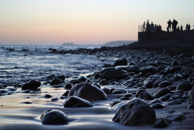 Surface level of pebble beach against sky during sunset