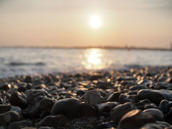 Surface level of pebble beach against sky during sunset