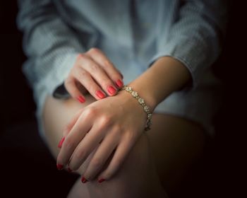 Midsection of woman with red nail polish and bracelet in darkroom