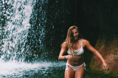 Young woman in bikini standing against waterfall