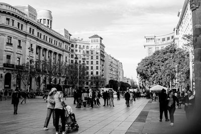 People walking on street amidst buildings in city against sky