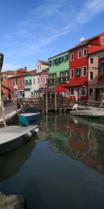 Boats moored in canal by buildings in city against sky