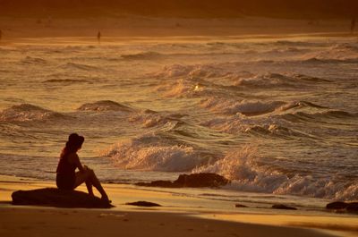 Woman sitting on beach against sky during sunset