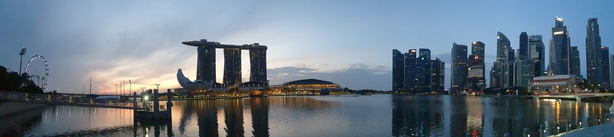 Illuminated buildings by river against sky in city