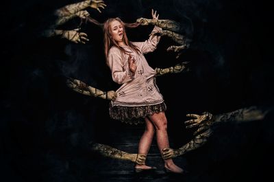 Portrait of young woman standing against black background