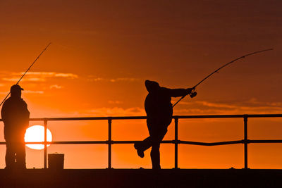 Silhouette man fishing by sea against sky during sunset