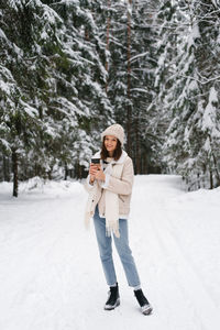 Young woman is standing in the snow with cup of coffee in her hand. concept of warmth and comfort