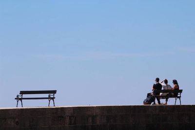People sitting on railing against clear sky