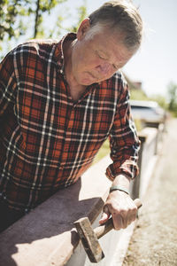 Senior man examining surrounding wall with hammer at yard