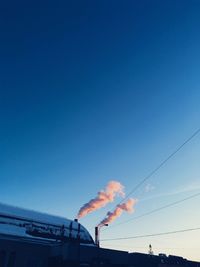 Low angle view of smoke stacks against clear blue sky