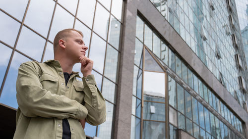 A pensive man stands against the backdrop of a skyscraper