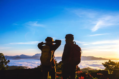 Friends standing on rock against sky during sunset